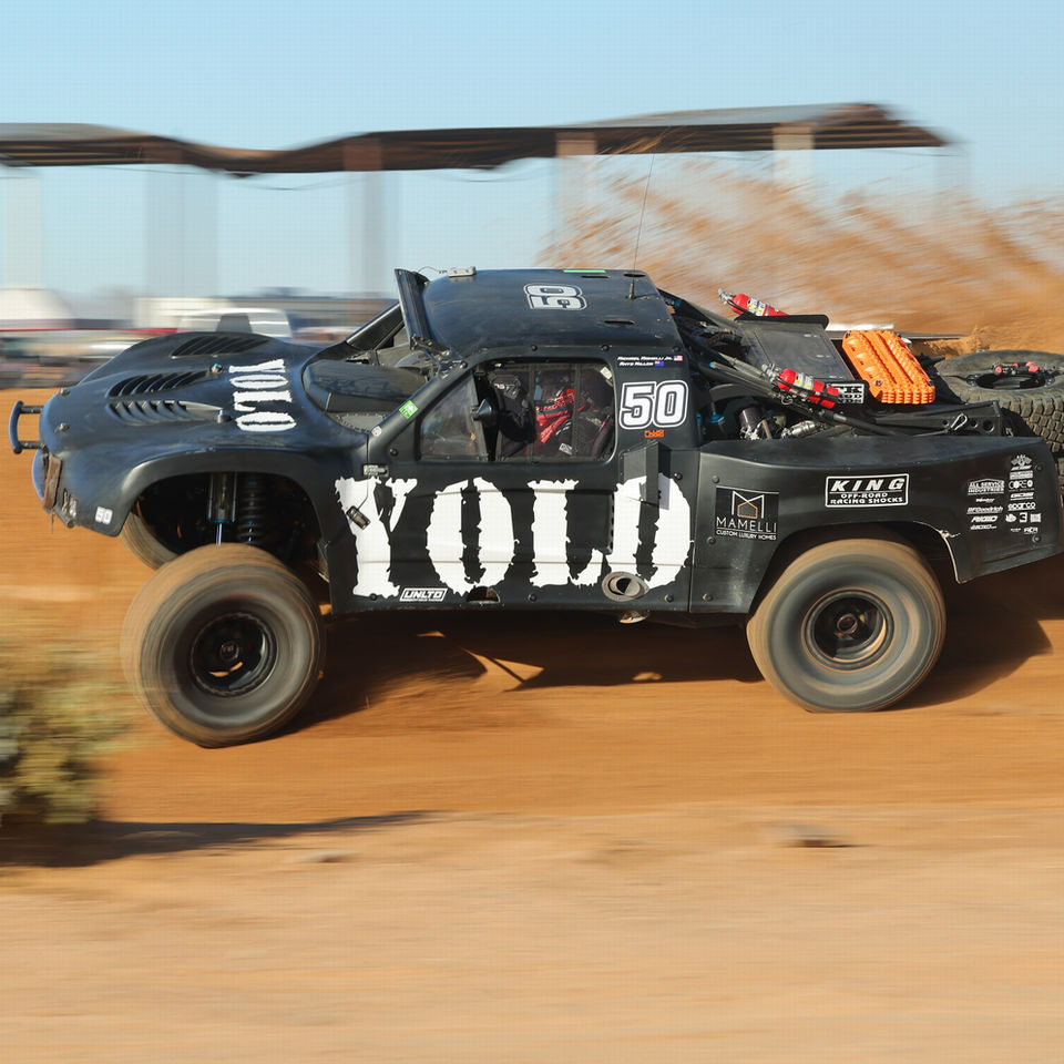 Black quad dirt racing car with a white "YOLO" logo  speeding on desert dirt track.