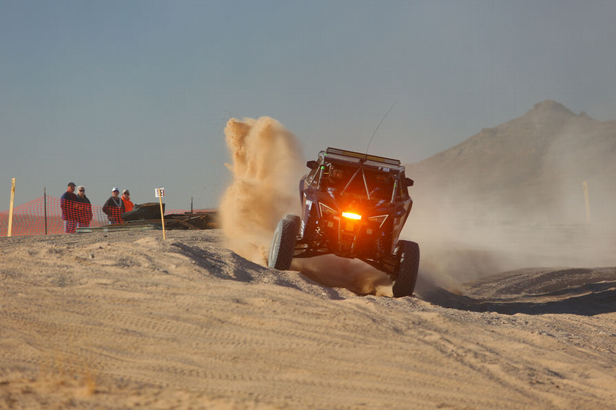 Black quad dirt racing car with an orange headlight speeding on desert dirt track.