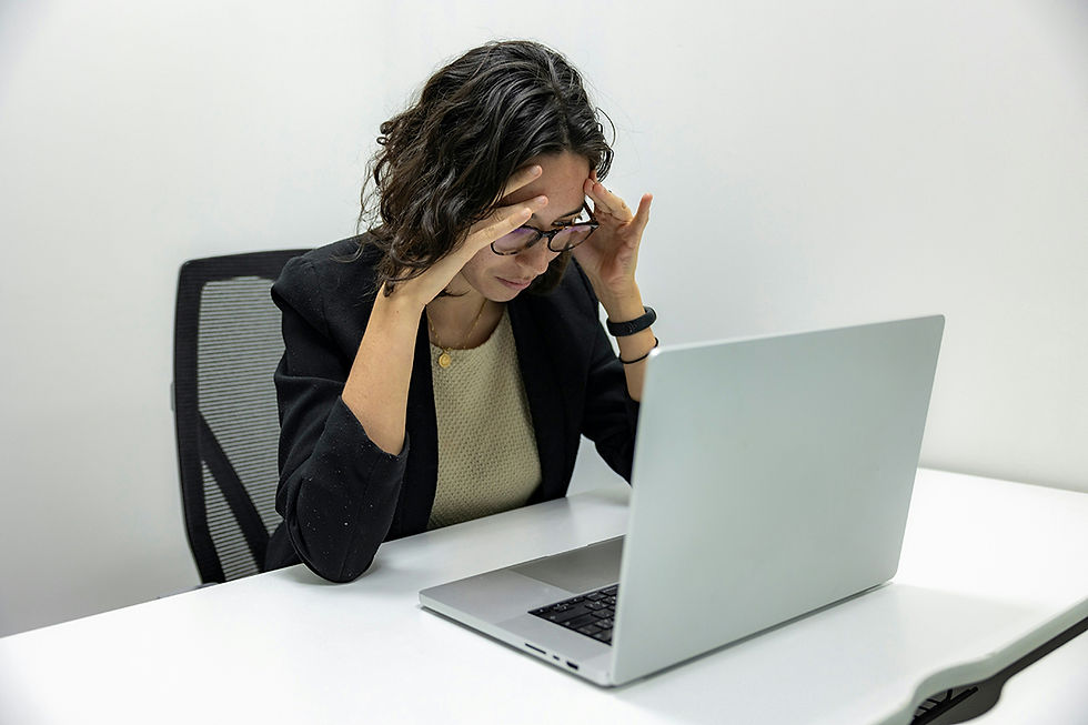 Woman sitting at a desk with her computer infant of her. Holding her head in her hands, with a disengaged look on her face