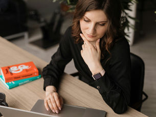 woman dressed in black office attire looking at a laptop