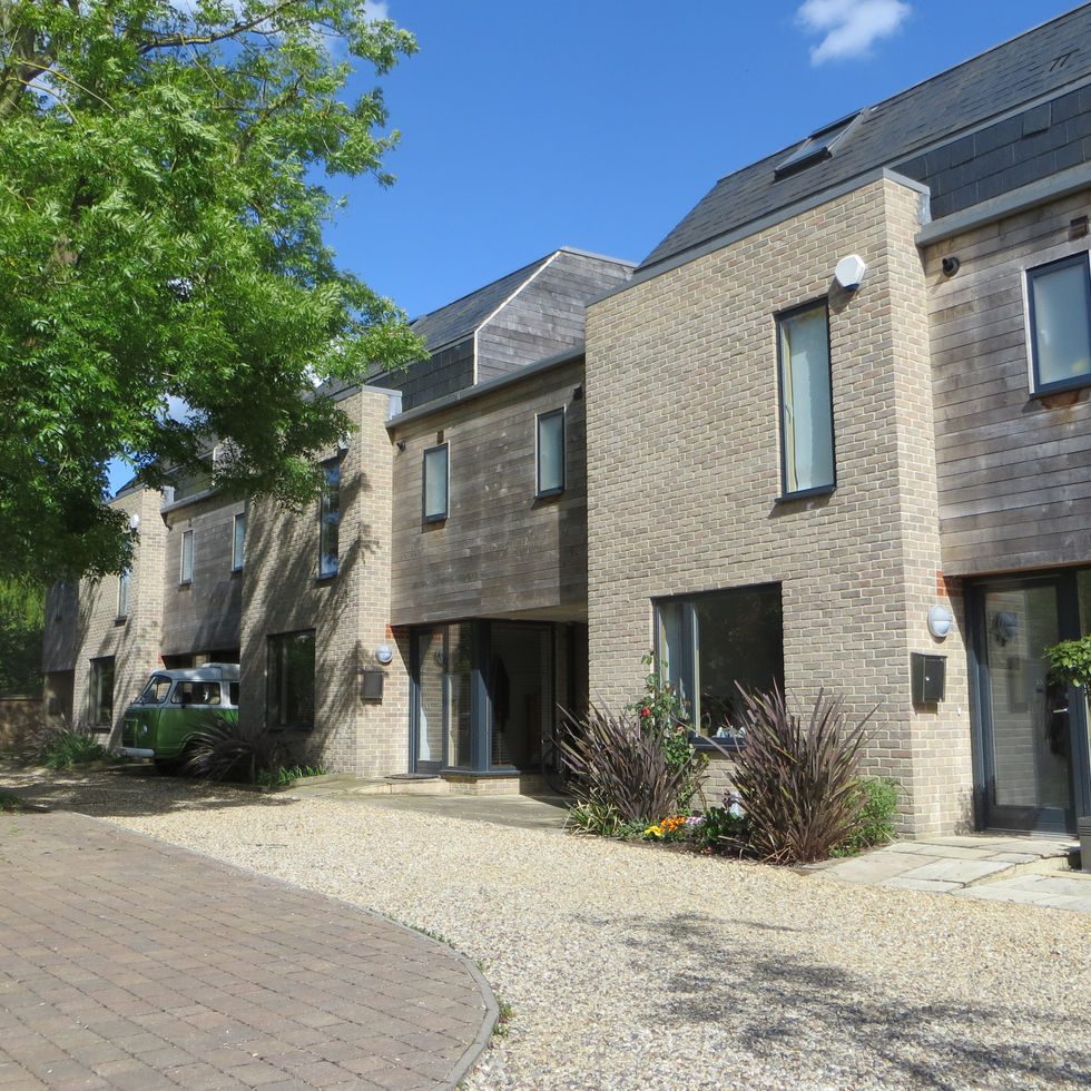 Architectural view of the communal lane at the Richmond Road mews residential development in Cambridge by Haysom Ward Miller Architects, featuring link-detached houses, landscaped gravel surfaces, and mature trees.
