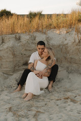a couple sitting and getting snuggly in the sand on the beach