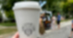 Close-up of a hand holding a Zemi Coffee cup with the logo, while guests enjoy the mobile coffee cart in the background.