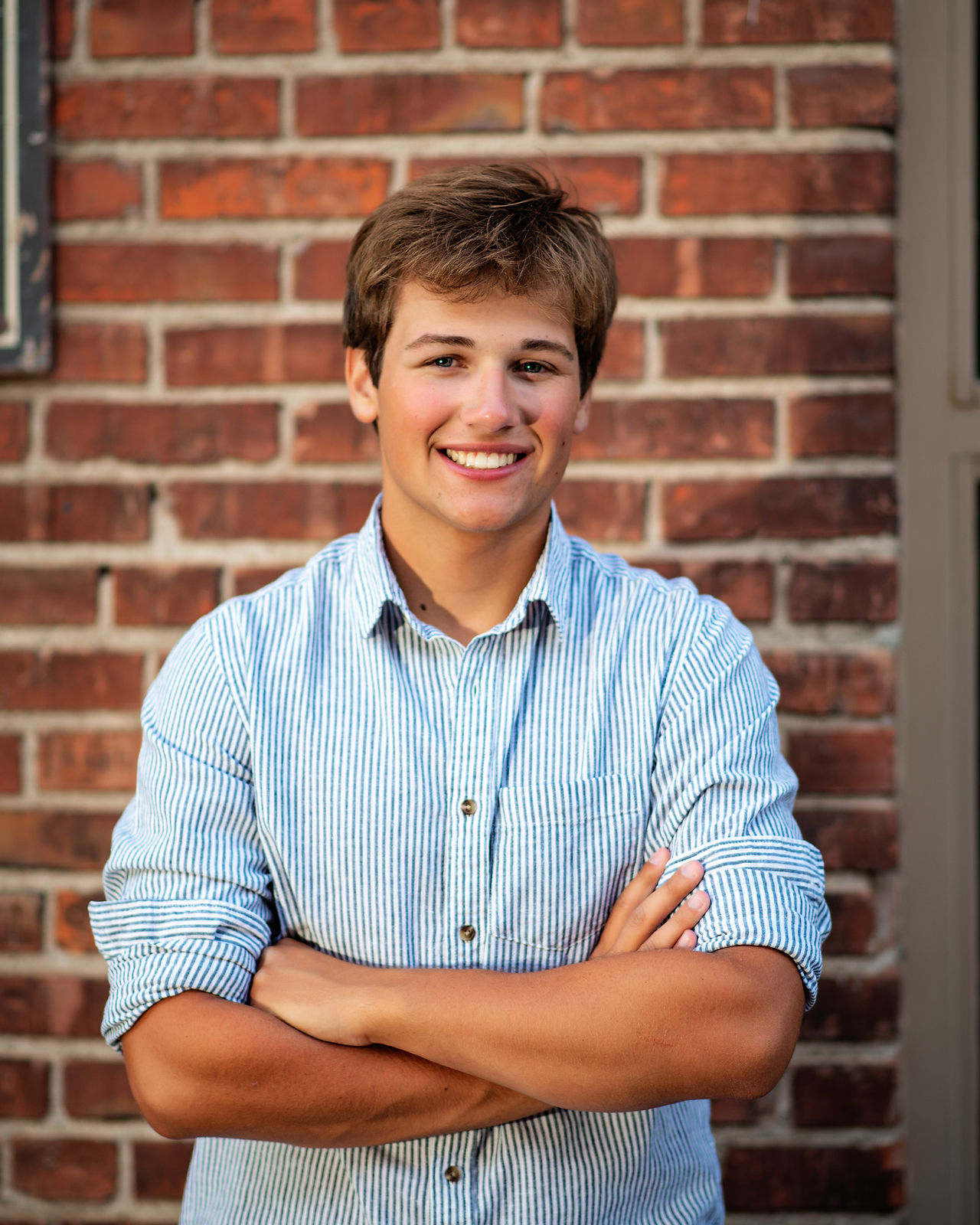 High School Senior boy smiling, standing near a brick wall