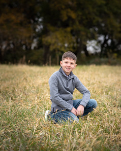 son smiles for camera in middle of field during Fall in Nebraska