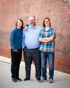Twin boys standing along a brick wall with their proud father. 