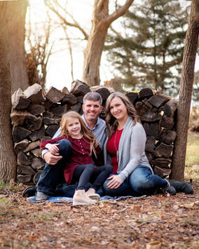 family sitting by a log pile at sunset