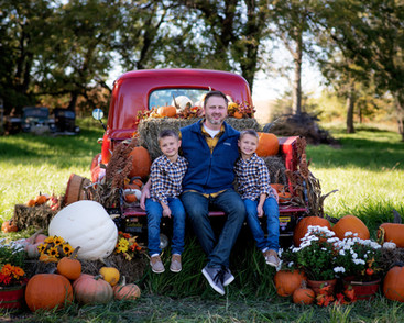 Father and sons sitting in pumpkin truck for fall