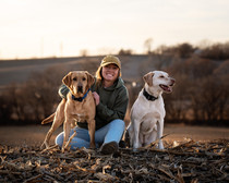 Envision K9 owner, Emilee Minnick sitting with her two working dogs in a field. 