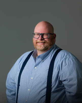 Business professional man stands smiling along a grey backdrop.