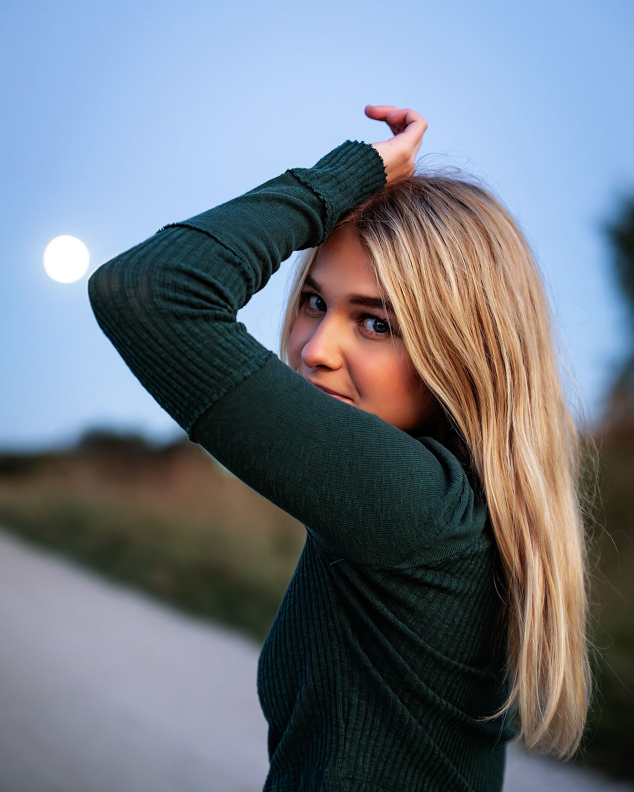 Girl standing on roadway for senior photos.  Setting sun radiating through trees for evening ambience.