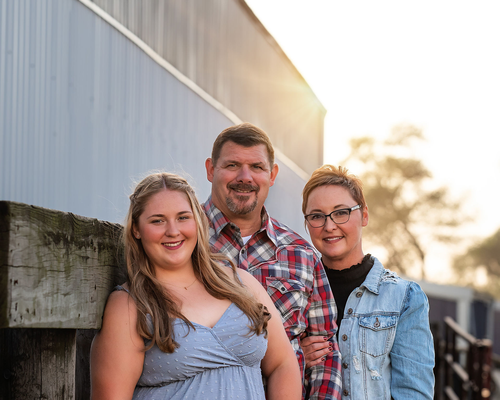 Senior girl leaning on fence line with her mom and dad