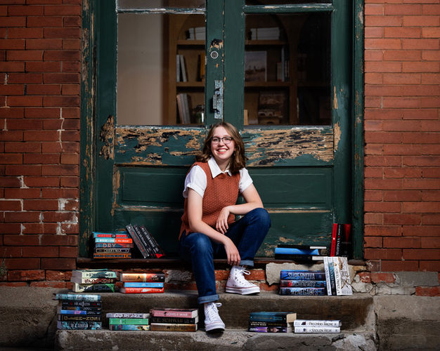 high school senior girl sits on a stoop with her books around her.
