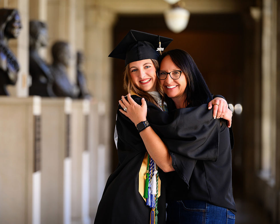 Nebraska high school senior in cap and gown embracing her mom in a columned hallway at the Nebraska Capitol Building in Lincoln, Nebraska