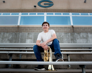 Senior boy sitting on stadium bleachers with baritone at Gretna High School