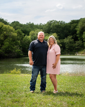 Man and wife standing in an open field in front of a lake for extended family photos.
