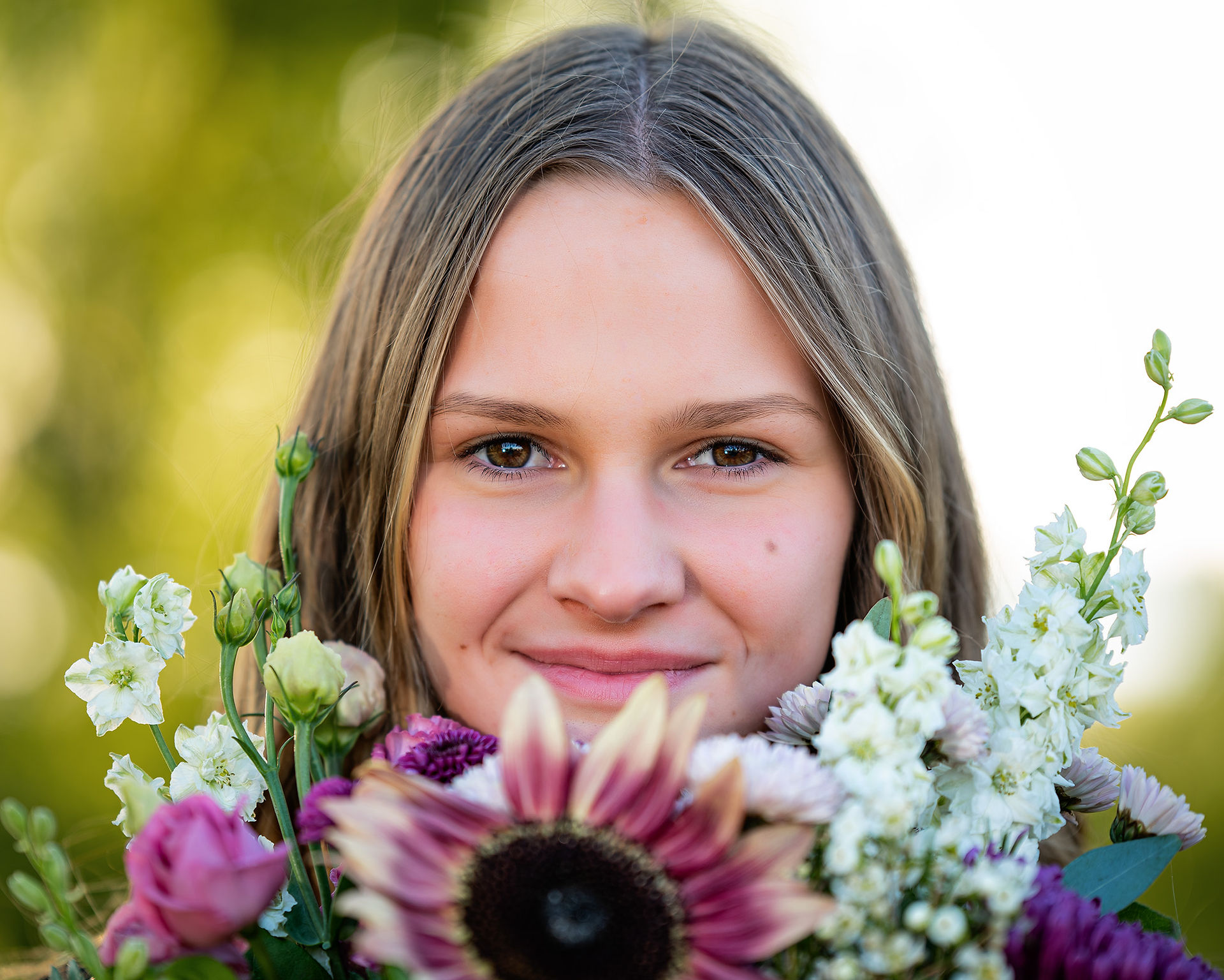 Senior girl smiling at the camera while holding a large wildflower bouquet. 