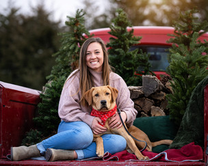 A gal sits with her dog in the back of a vintage pickup for a holiday photo.
