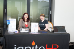 two ladies sit at the Ignite HR booth at a networking event.