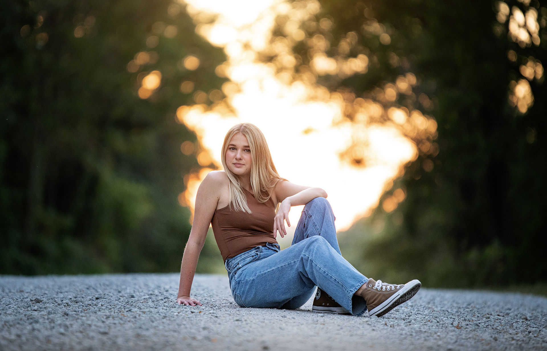 Senior girl sits in middle of country road. 