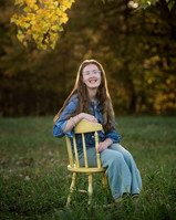 Young daughter sitting on a chair in an open field for family portraits.