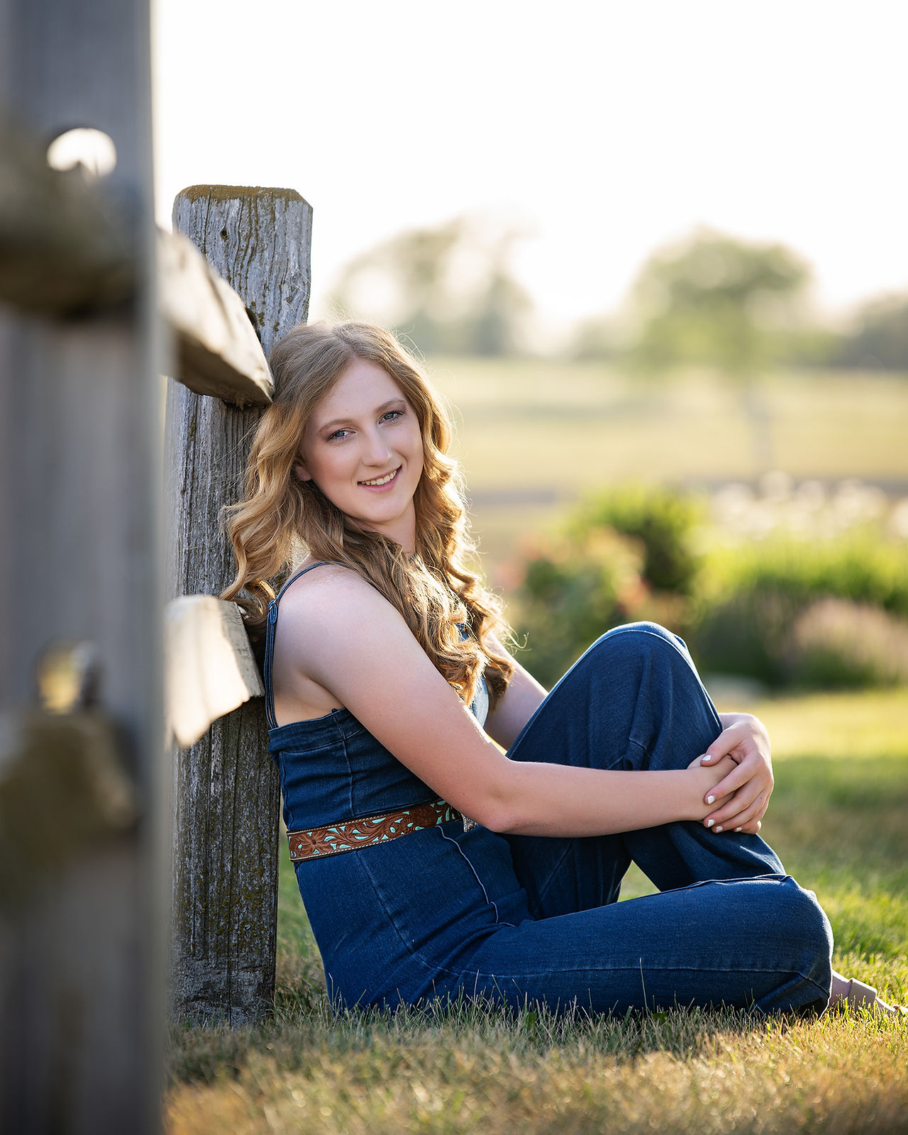 Senior girl sitting against wooden post on a summer day.