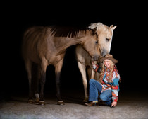 Young teenage girl laughing while kneeling in front of her two horses. 