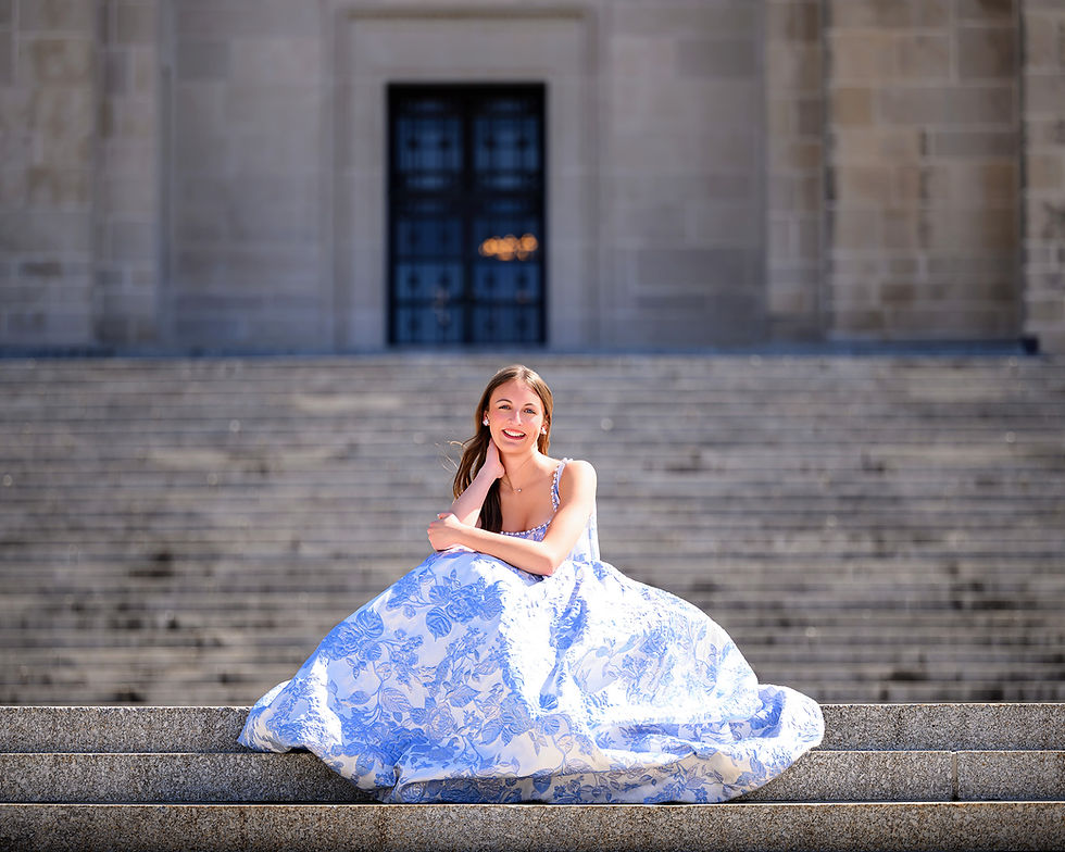 Nebraska high school senior Riley in a blue and white floral gown sitting on the front steps of the Nebraska Capitol Building in Lincoln, Nebraska