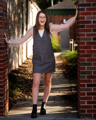 Nebraska senior girl in jumper leaning on urban brick wall