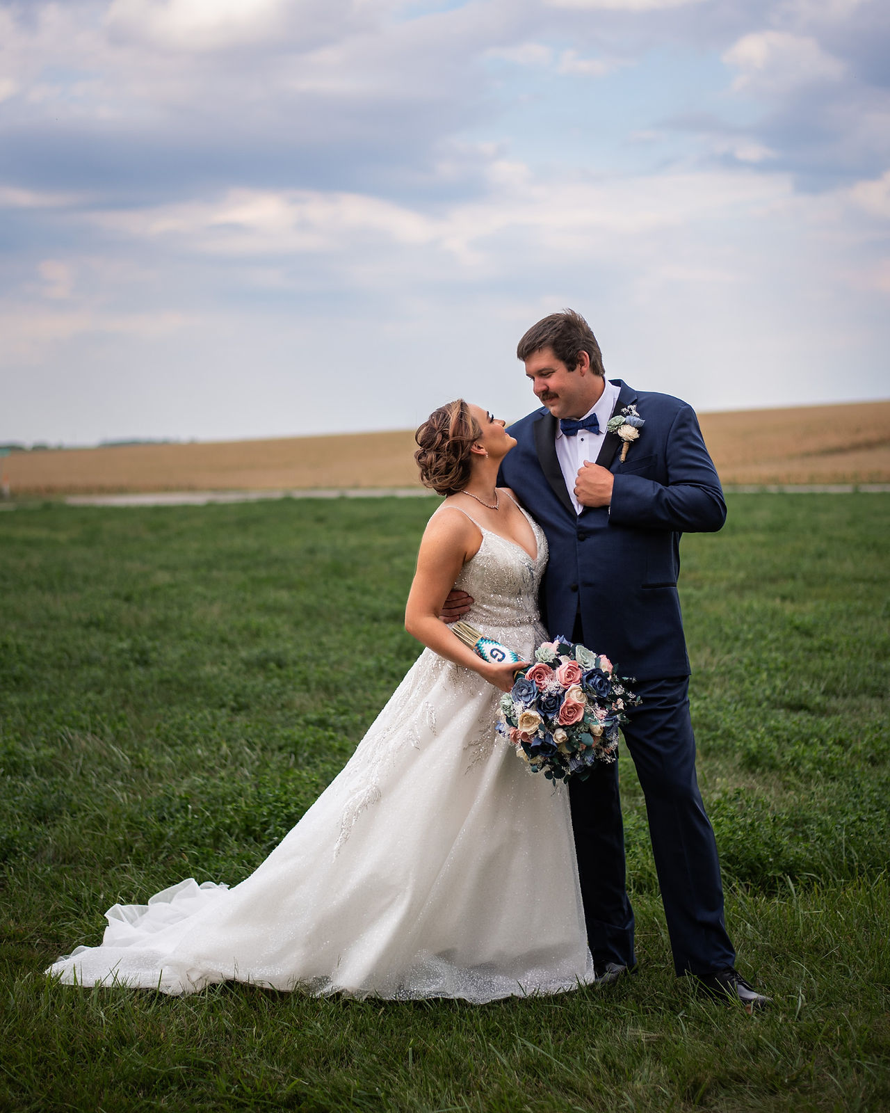 Bride and groom looking at each other while standing in a field in summer 