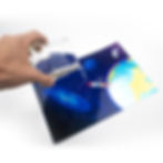 A hand pouring water to A4 Holographic Silver Sticker Vinyl Label featuring a spaceman tethered to a colorful earth.