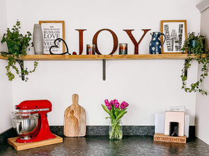 Metal letter spelling JOY sitting on a scaffolding shelf in a kitchen above a red Kitchenaid mixer