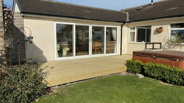 Rear view of a house showing bi fold doors opening onto a light timber deck and lawn