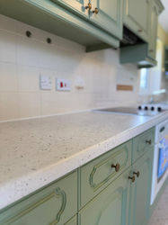 A kitchen with light green cabinets and a speckled countertop