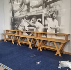 Multi-level wooden trestle tables by the wall of images of cricketers