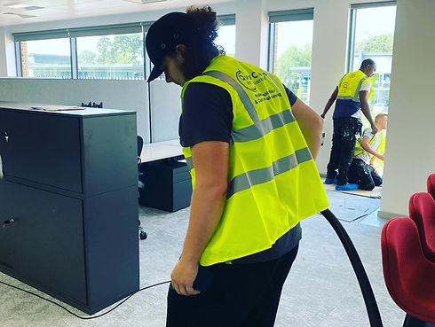 Man in hi-vi cleaner vest vacuuming a room