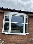 A newly installed grey window overlooks a lush garden, with tools scattered in the room and a level leaning against the wall.
