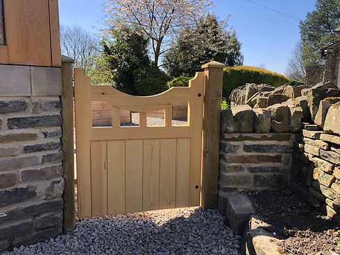 Small curved wooden garden gate set into a rustic stone wall