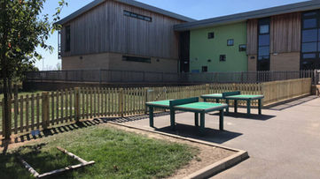 Outdoor school playground area with green table tennis tables and a timber picket fence border