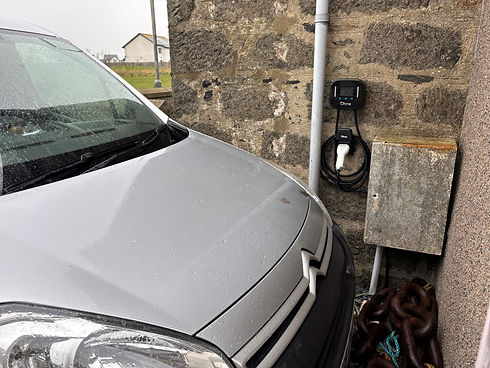 Front of a silver car parked next to a wall mounted Ohme EV charging unit with connected cable