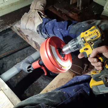 Plumber drilling a hole in the underfloor pipe