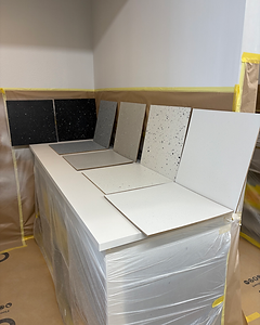 Kitchen worktop samples displayed during installation, showing white, speckled, and dark countertop options on a protected cabinet unit.