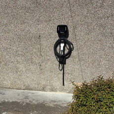 Black electric vehicle charging point mounted on an outdoor stone wall near green shrubs