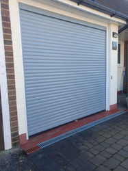 Front-facing view of a white roller shutter garage door framed by brick walls and paving stones.