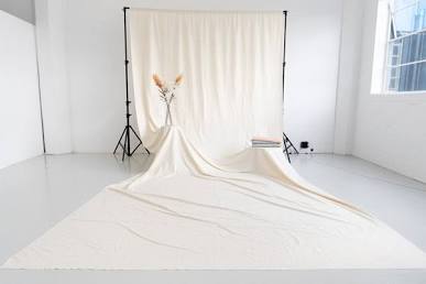 A wrinkled, cream-colored muslin backdrop draped over a stand in a photography studio, showing uneven shadows.
