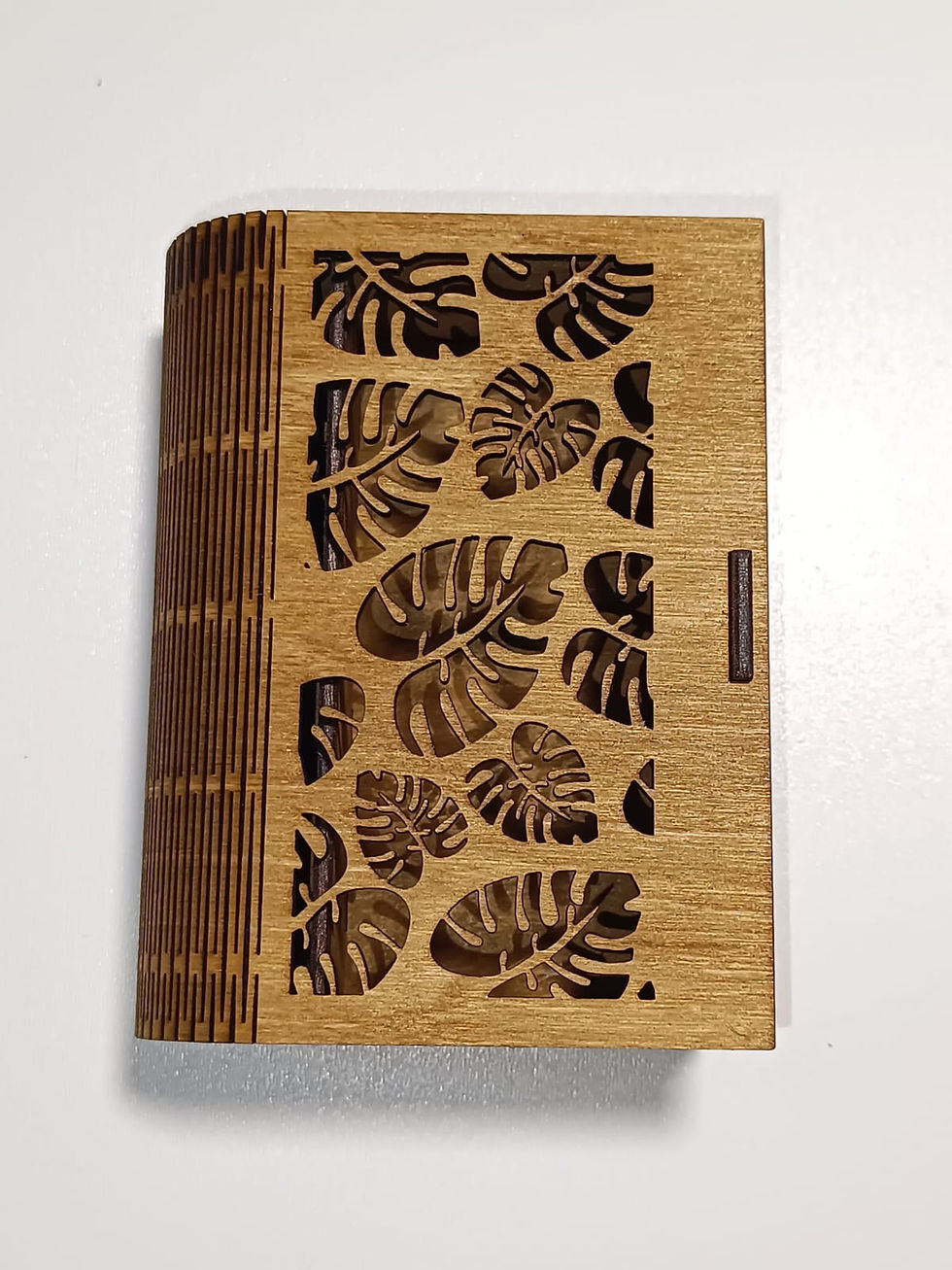 Dřevěná šperkovnice s laserem vyřezávaným vzorem listů monstera, focená z horního pohledu. Vyniká preciznost řezu.