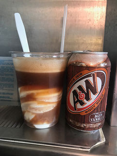 A classic root beer float made with A&W root beer and creamy vanilla soft serve, served in a clear plastic cup with a straw.