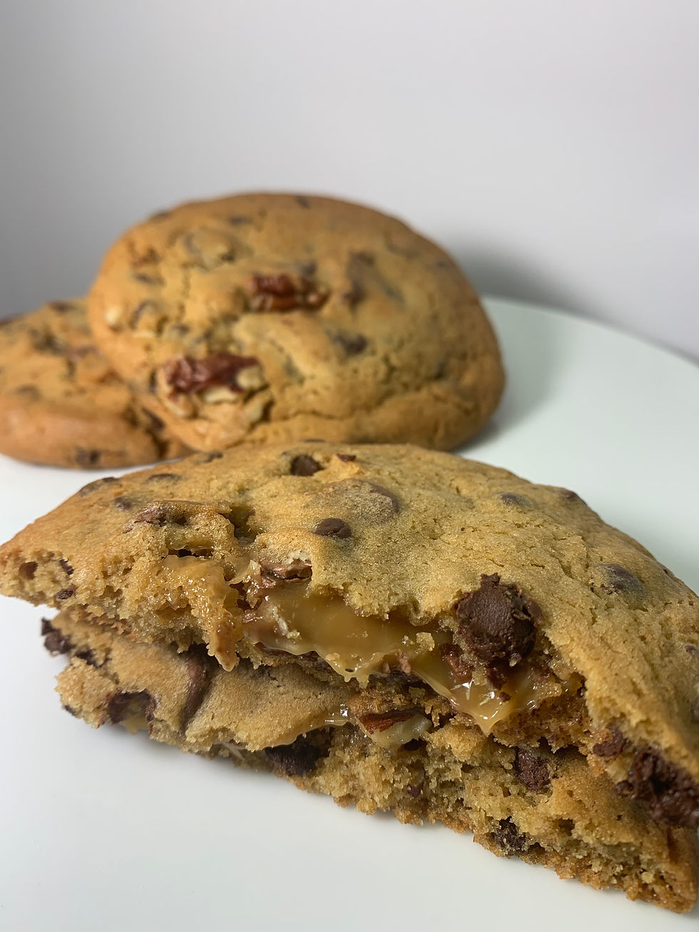 Thumbnail: The Nookie Cookie broken in half to reveal the gooey caramel center, with chocolate chips and pecans.