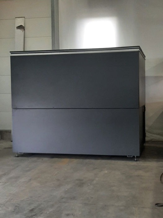 Große, graue Industriemaschine auf Betonboden in einer Halle.