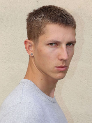 Serious young man in grey t-shirt with short hair, ear piercing.